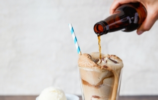 Someone's hand pouring root beer into a root beer float