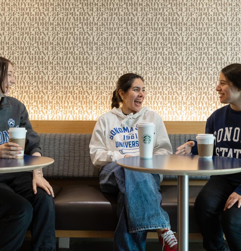 Three students sitting and talking at Sip dining venue with coffee cups on the tables