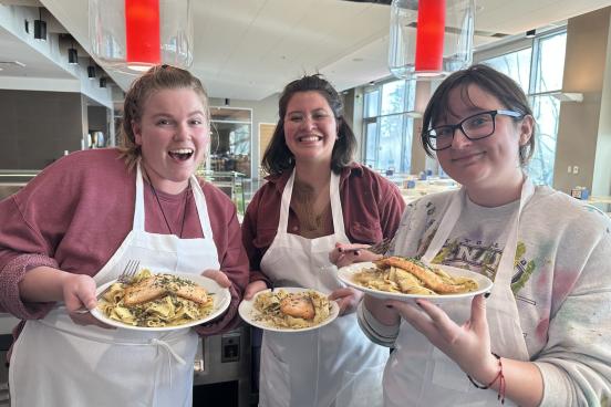 Three students pose with their cooking creation of salmon and pasta on plates