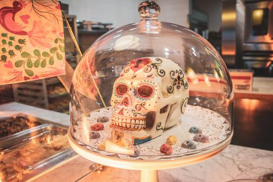 A white sugar skull with colorful decoration inside a glass domed pastry case