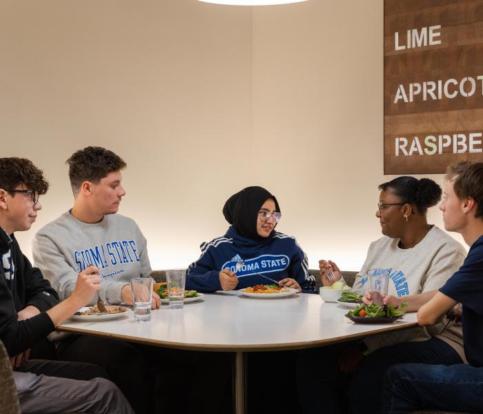 Group of five students sitting at a table talking and eating food