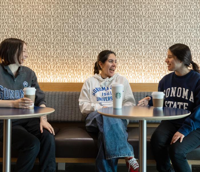 Three students sitting and talking at Sip dining venue with coffee cups on the tables