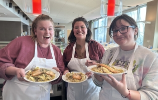 Three students pose with their cooking creation of salmon and pasta on plates