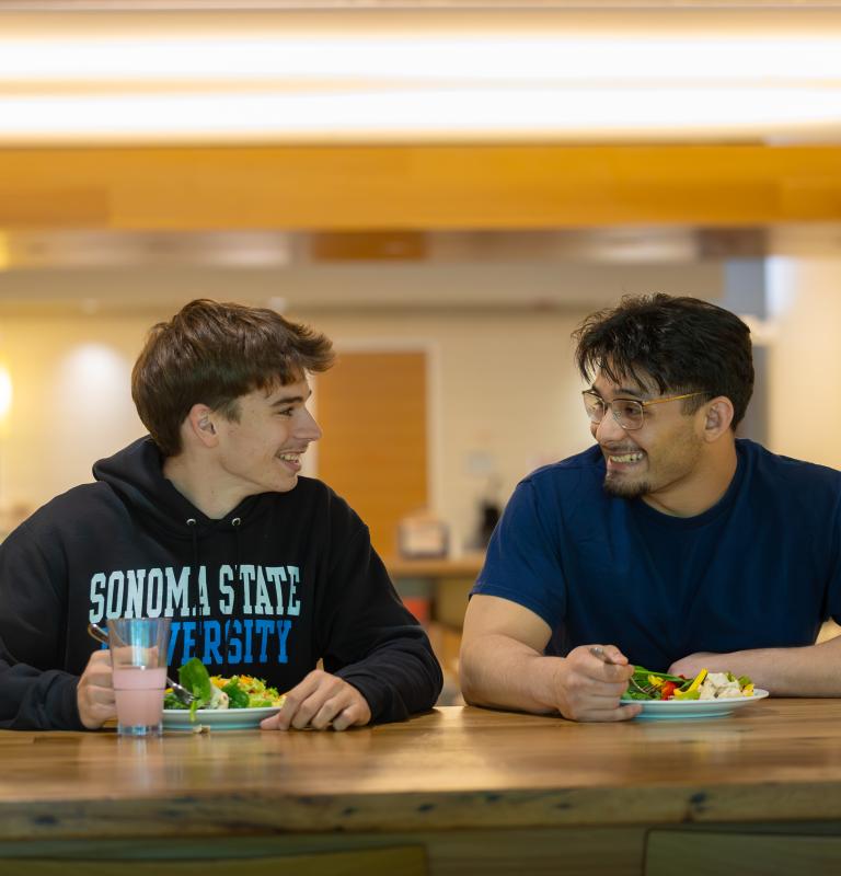 Two students looking at each other with plates full of food in the dining hall The Kitchens