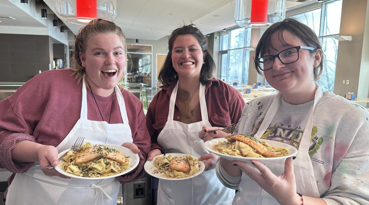 Three students pose with their cooking creation of salmon and pasta on plates