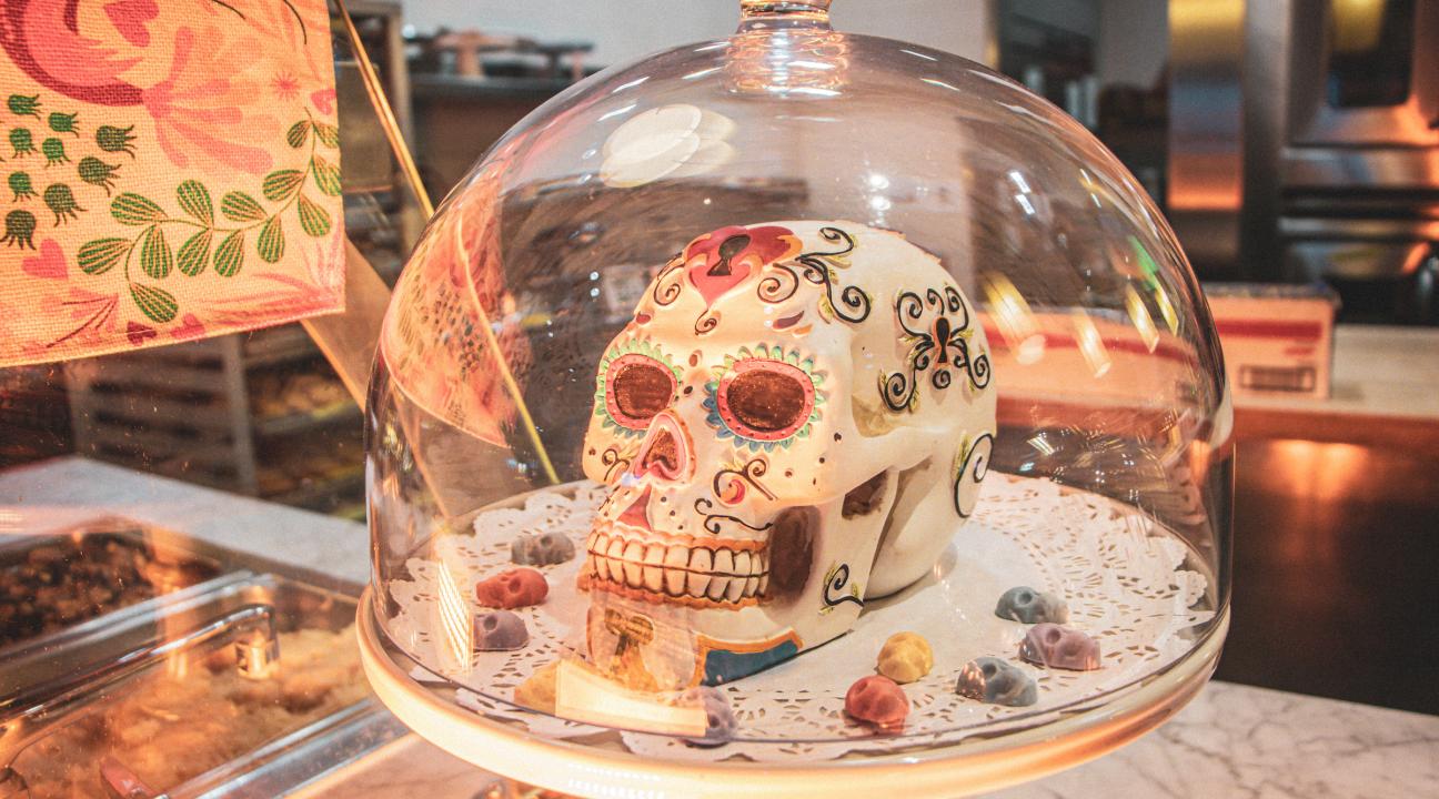 A white sugar skull with colorful decoration inside a glass domed pastry case