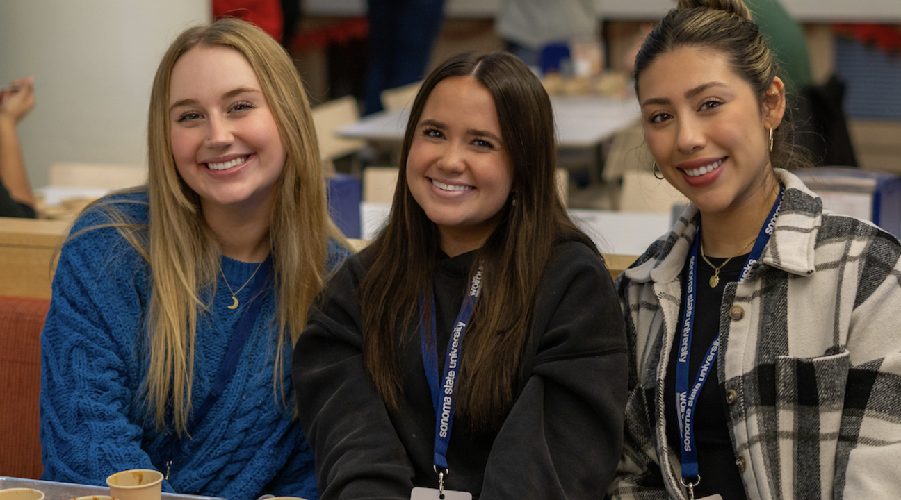 three students tasting chili and smiling