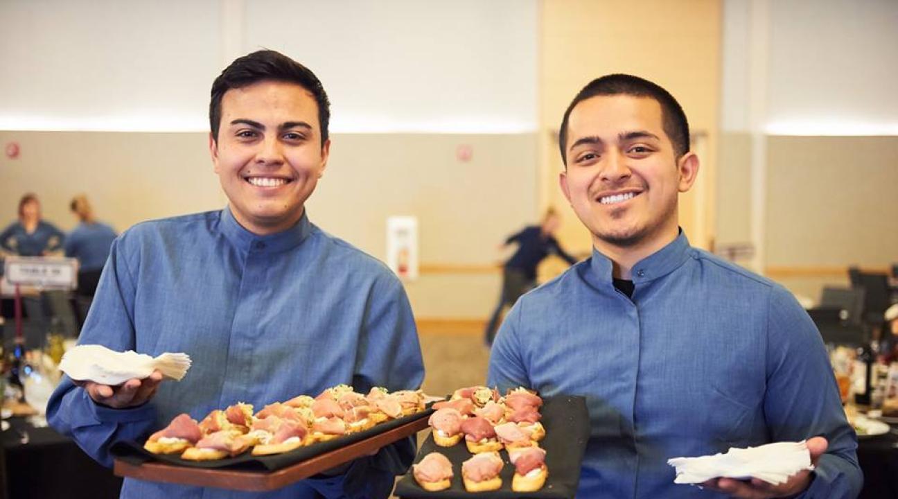 Two students holding catering trays of food 