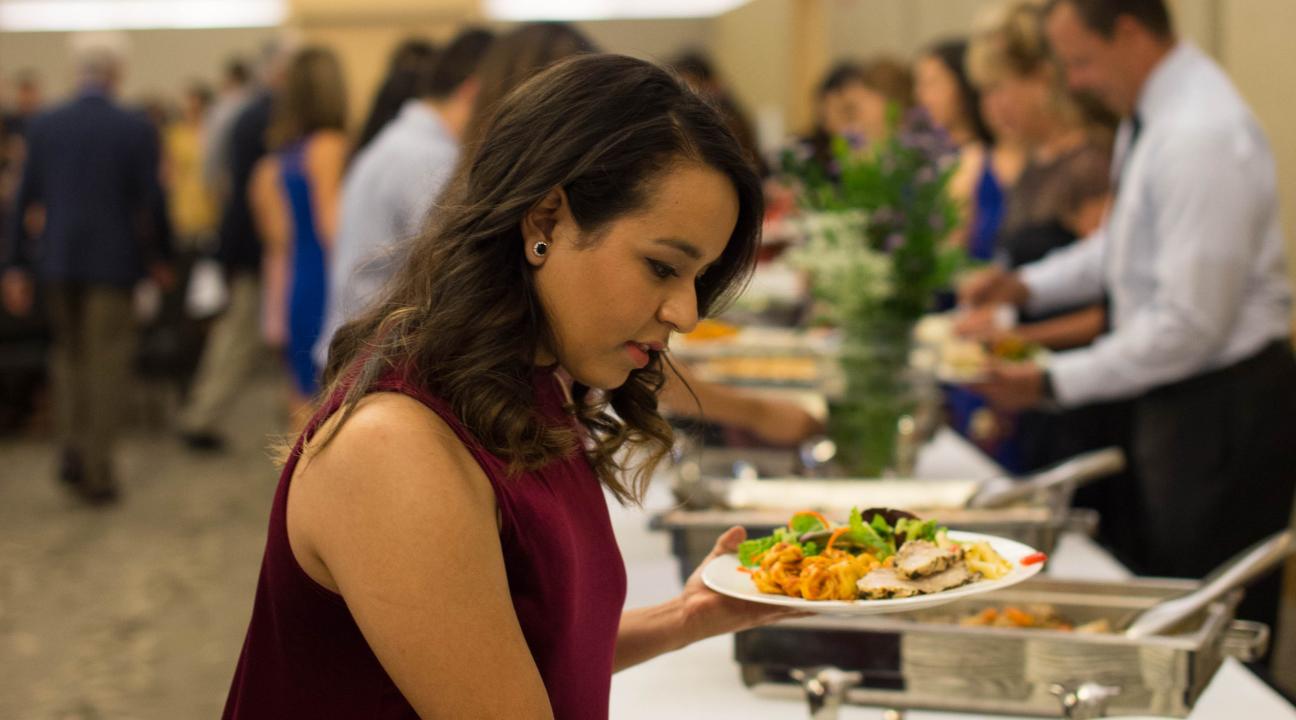 Person holding plate of food and grabbing more food with tongs 