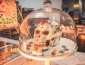 A white sugar skull with colorful decoration inside a glass domed pastry case
