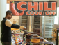 a student serving himself chili from the table with the chili cook off banner in background