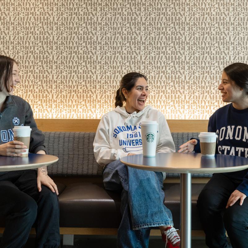 Three students sitting and talking at Sip dining venue with coffee cups on the tables