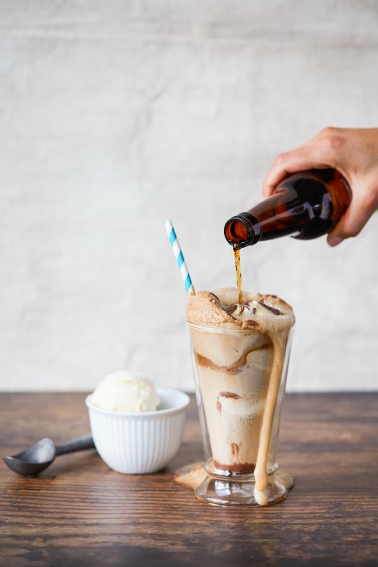 Someone's hand pouring root beer into a root beer float