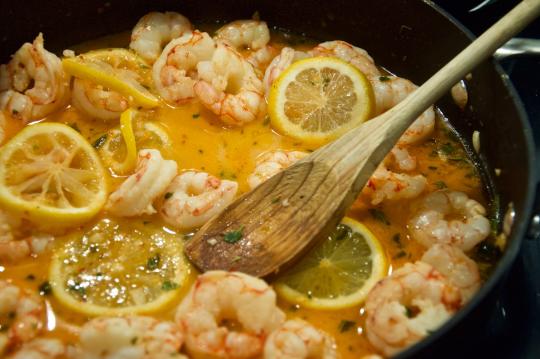 lemons and shrimp cooking in a pan with a spoon