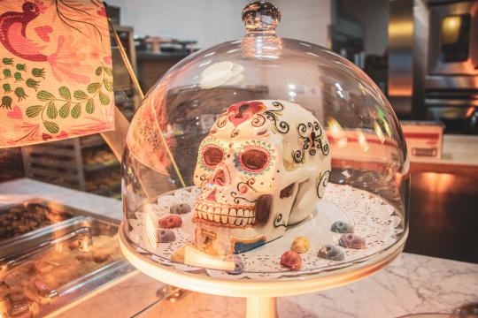 A white sugar skull with colorful decoration inside a glass domed pastry case