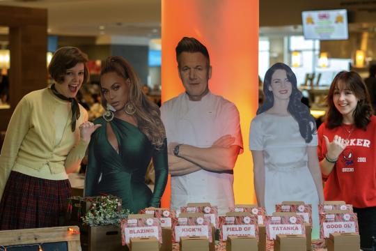 two students posing near the voting area with cut outs of Beyonce, Gordon Ramsay, and Lana Del Rey