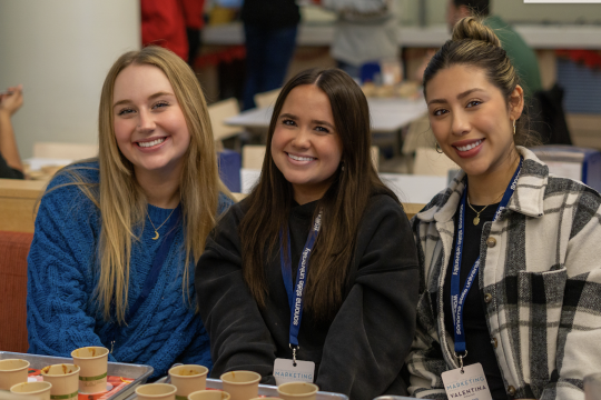 three students tasting chili and smiling