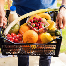 Person holding a box of vegetables, fruit and milk