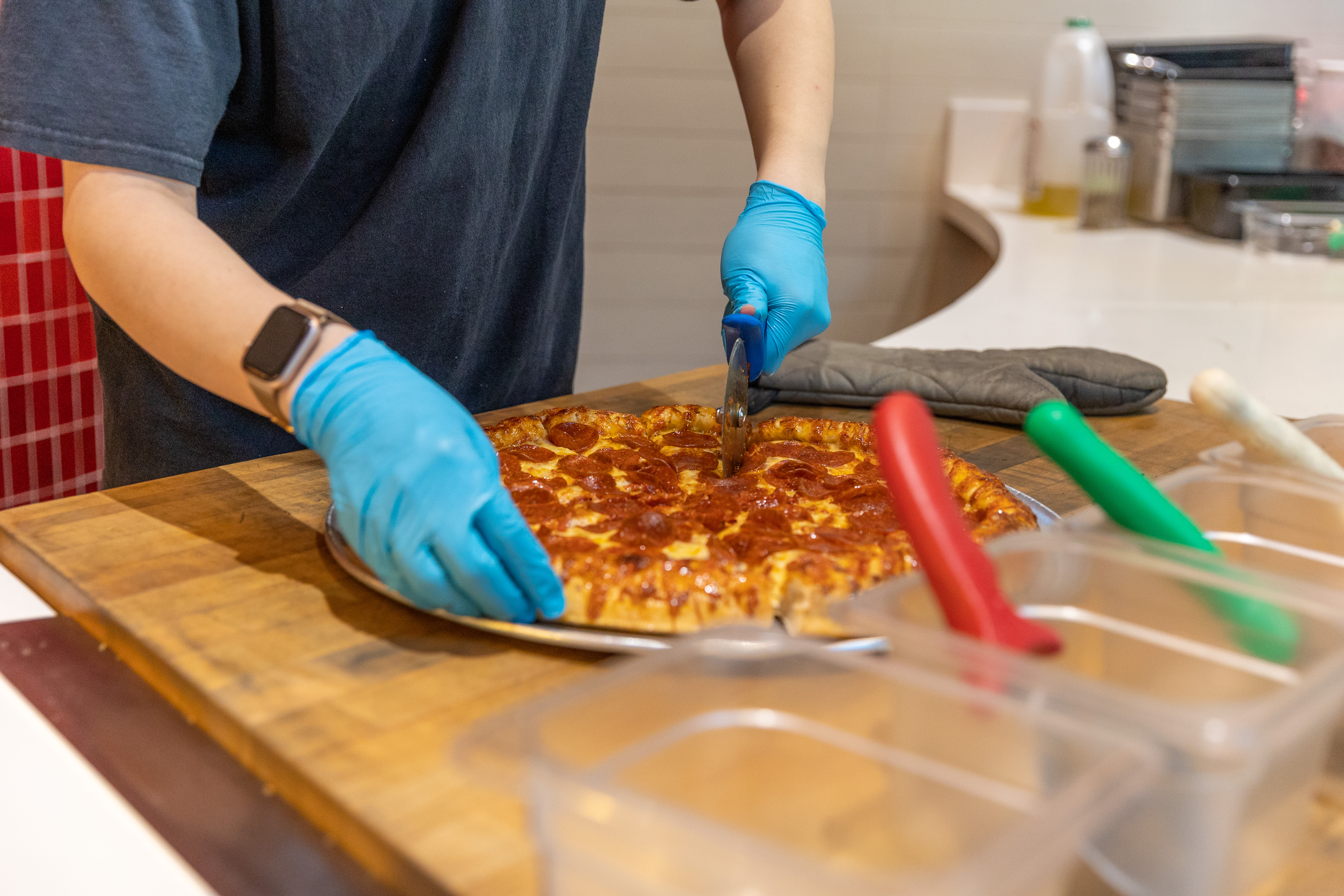 Hands in gloves cutting pizza