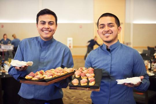 Two students holding catering trays of food 