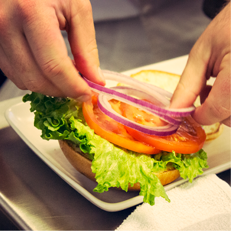 someone putting vegetables on burger